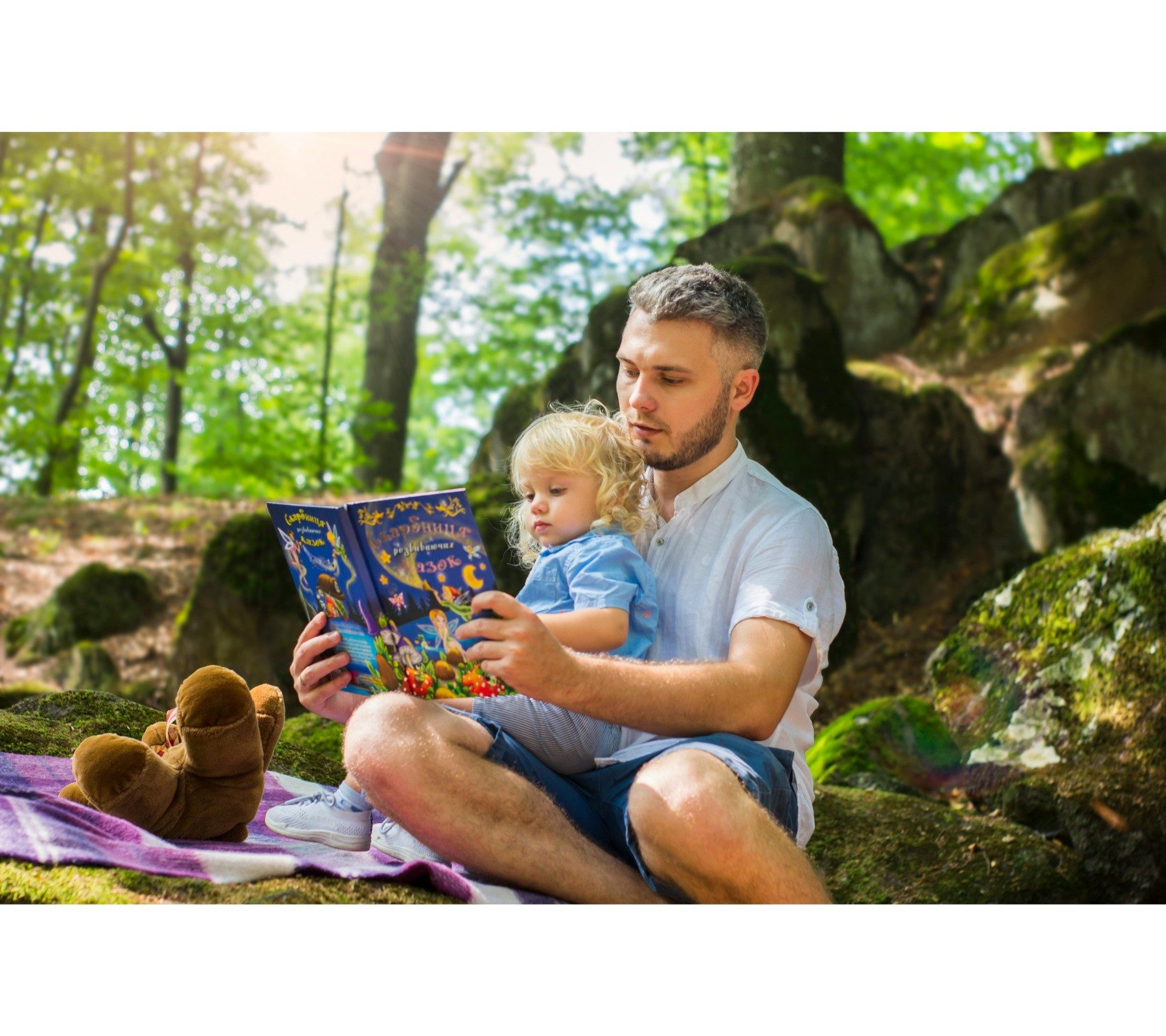 Man reading book to toddler in forest