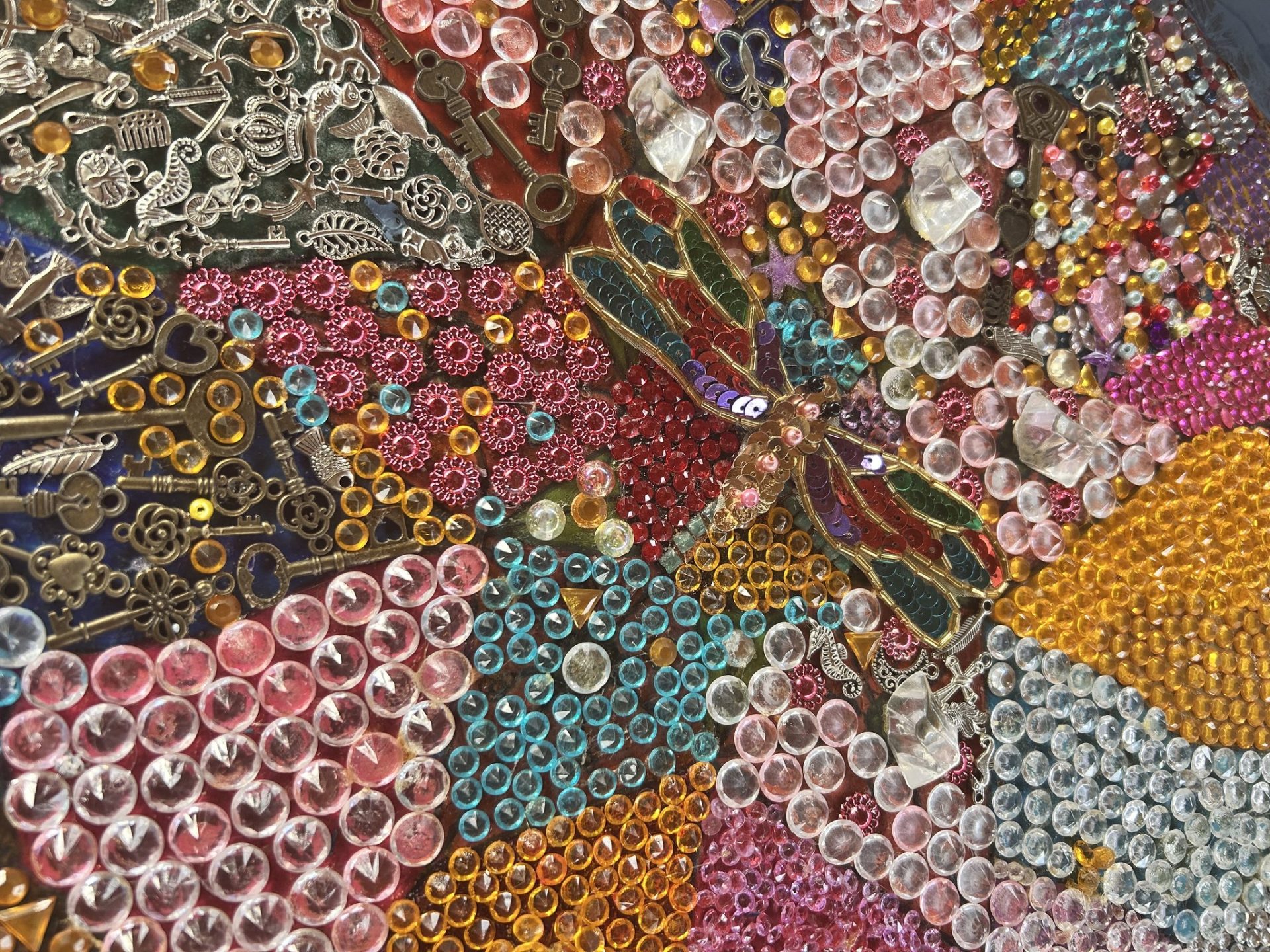 Dragonfly made out of sequins embossed on colourful background made out of coloured glass