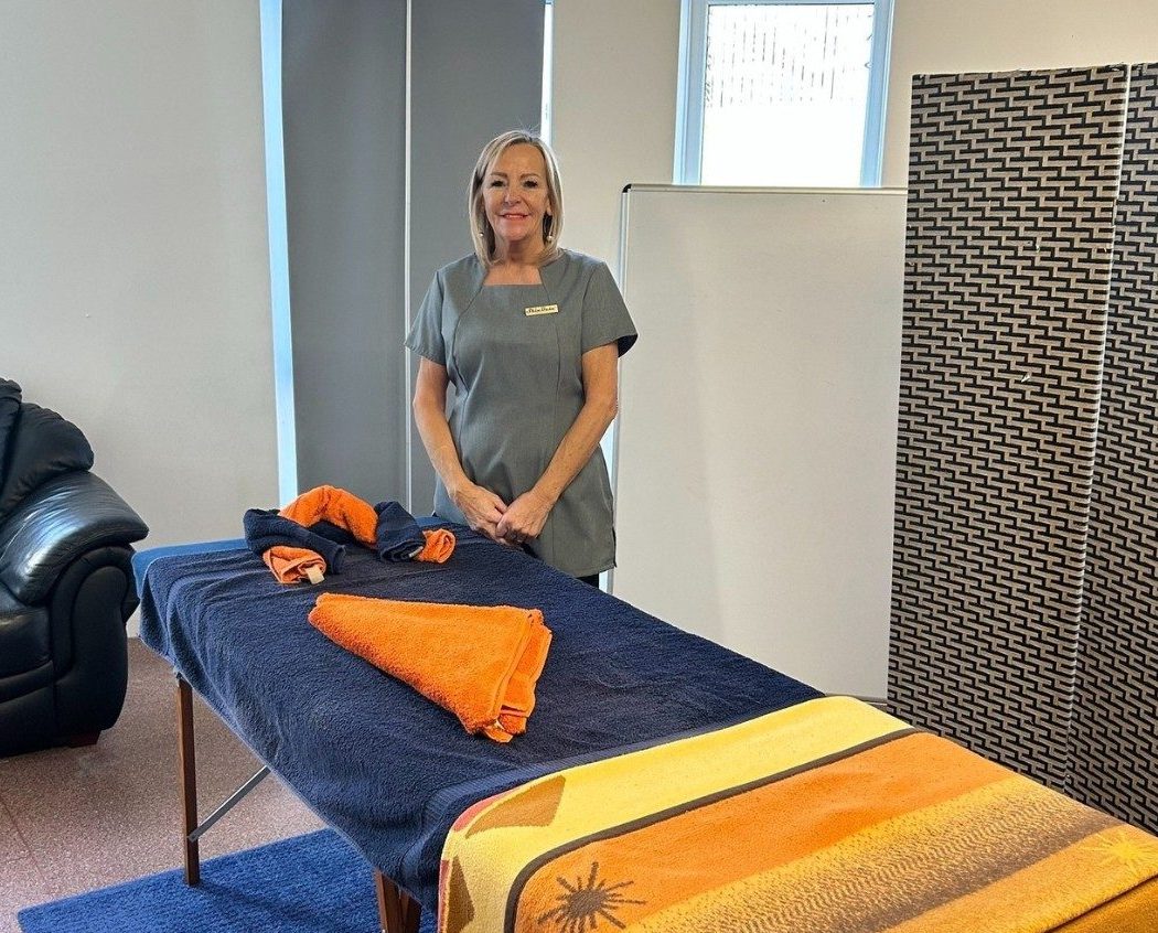 Massage therapist Karen stood behind massage bed