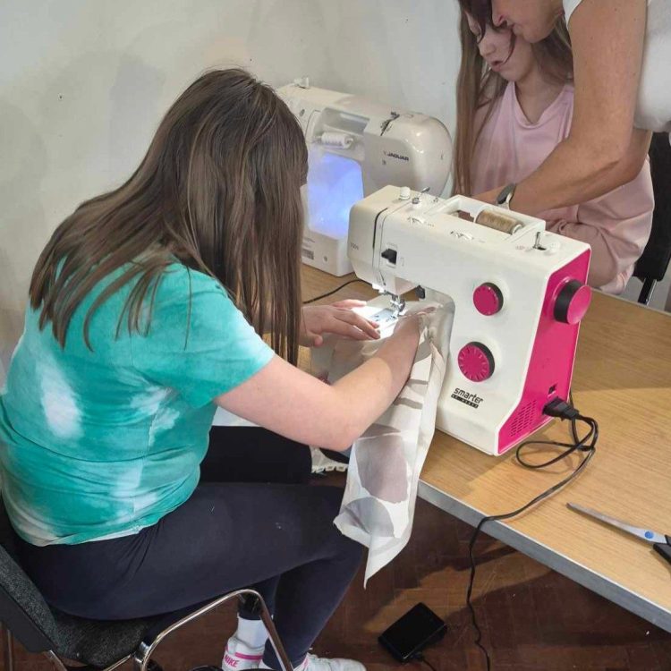 Two young girls using sewing machines with help