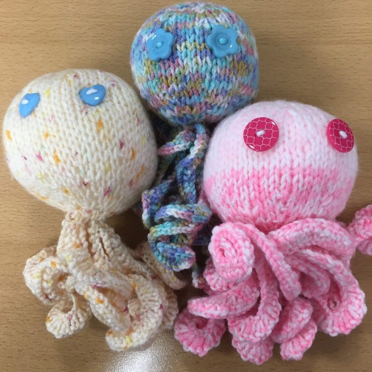 Three knitted octopus. One pink, one yellow and one grey. All knitted by Sunderland Mind Fabric Creations Member