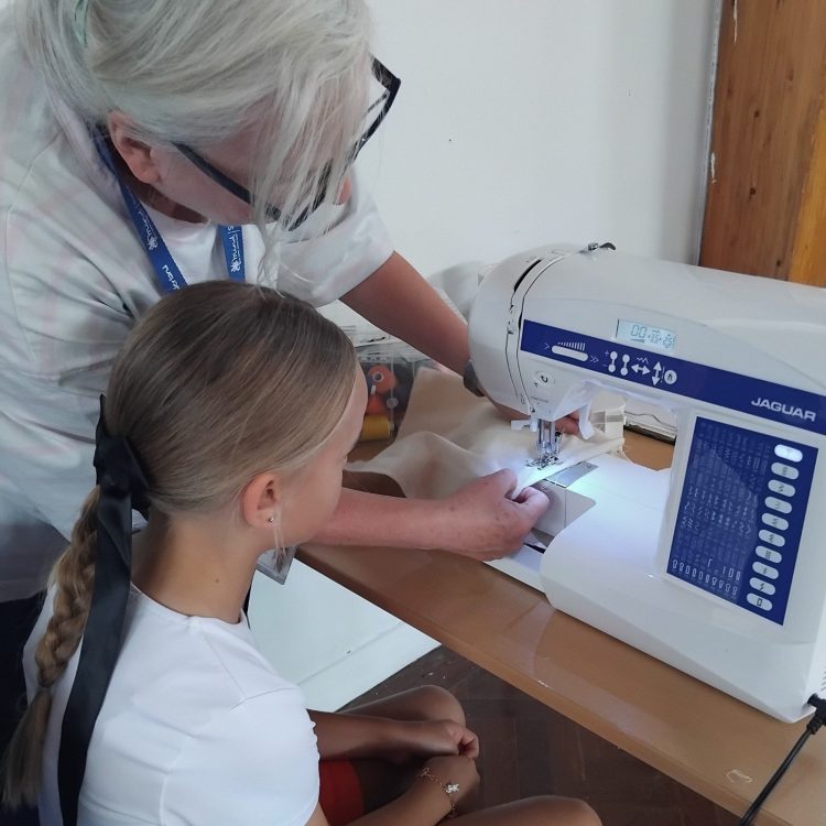Volunteer teaching young person to sew